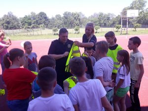 Policjantka wspólnie ze strażnikiem gminnym rozdają dzieciom kamizelki odblaskowe.