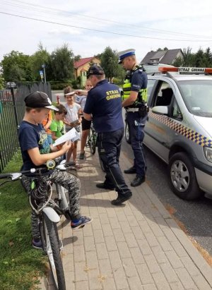 funkcjonariusz Policji Straży Gminnej wręczają elementy odblaskowe pieszym