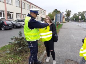 Policjant ruchu drogowego w trakcie działań NURD przekazuje kamizelkę odblaskową pieszej