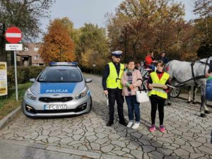 policjant ruchu drogowego wspólnie z druhną z OSP Raciążek przekazują pieszemu element odblaskowy