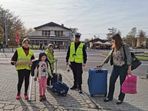 Policjant ruchu drogowego przekazuje pieszym elementy odblaskowe wspólnie z druhną z OSP