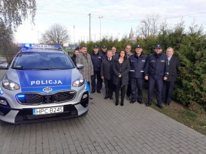 Policjanci wspólnie z zaproszonymi gośćmi stoją przy nowozakupionym radiowozie