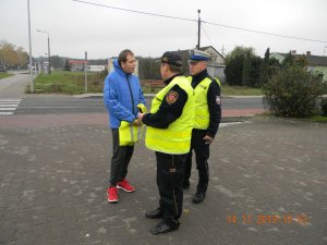 Policjant wspólnie,ze strażnikiem przekazują kamizelkę odblaskową pieszemu