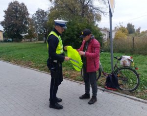 policjant przekazuje rowerzyście kamizelkę odblaskową