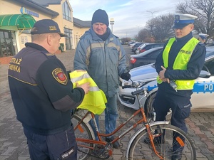 policjanci wspólnie ze strażą przekazują kamizelkę rowerzyście