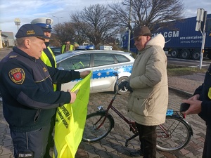 policjanci wspólnie ze strażą przekazują kamizelkę rowerzyście