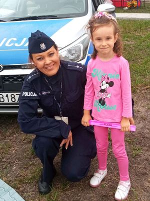 Policjantka stoi z dziewczynką przy radiowozie, uśmiecha się