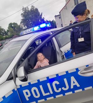 dziecko siedzi w radiowozie policyjnym, obok stoi policjantka