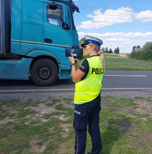 Policjantka stoi z urządzeniem do pomiaru prędkości w tle pojazd ciężarowy