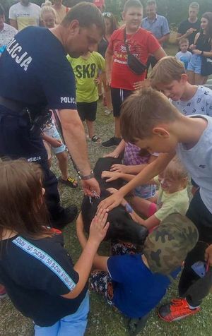 policjant stoi z psem policyjnym pośród dzieci