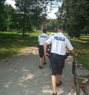 policjanci prowadza rowery alejką w parku