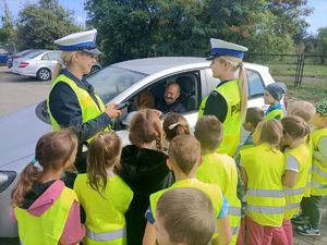 kierowca siedzi w aucie, koło auta stoją dzieci i policjantki