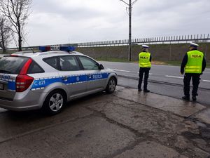 policjanci stoją na drodze przy radiowozie obserwują ruch na drodze