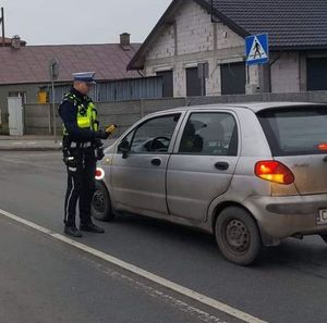 Policjant stoi przy aucie trzyma w ręku urządzenie do kontroli stanu trzeźwości