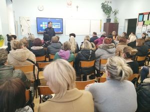 rodzice siedzą w klasie w tle stoi policjantka