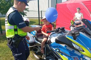 policjant stoi przy motorze na którym siedzi mały chłopiec