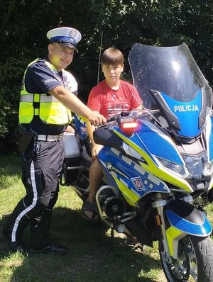 policjant stoi przy motocyklu na którym siedzi chłopiec