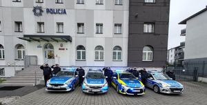 radiowozy z włączonymi sygnałami stoją przed jednostka obok nich policjanci