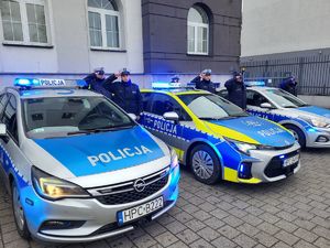 dwa radiowozy na sygnałach obok stoją policjanci