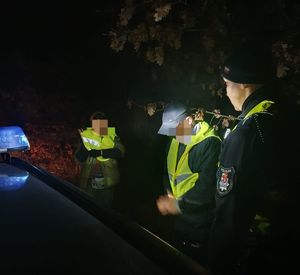 pora nocna , policjanci stoją przy dwóch osobach w kamizelkach