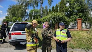 policjant ze strażakiem i żołnierzem stoją przy wozie strażackim