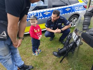 policjant pochyla się do dziecka w tle motocykl