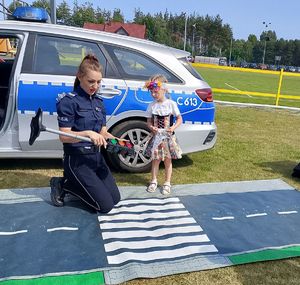 dziewczynka przy radiowozie z policjantkom przechodzi przez matę drogową