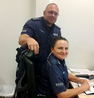 przy biurku siedzi policjantka za nią stoi policjant