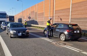 dwóch policjantów na drodze stoją przy pojazdach