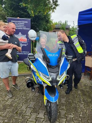policjant stoi koło motocykla na którym siedzi dziecko