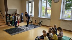 Policjantka rozmawia z dziećmi stojącymi przy macie drogowej