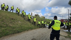 policjant przy wale powodziowym w tle wojsko układa worki z piaskiem