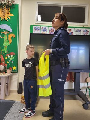 policjantka pokazuje dzieciom kamizelkę odblaskową