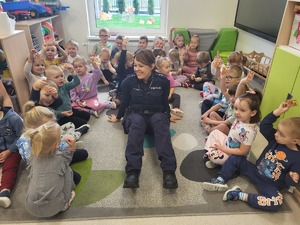 policjantka siedzi pośród dzieci, które trzymają odblaski