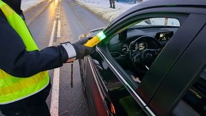 policjant trzyma alkomat i podsuwa kierowcy w stronę otwartego okna od auta