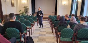 policjantka stoi pomiędzy krzesłami na których siedzi młodzież