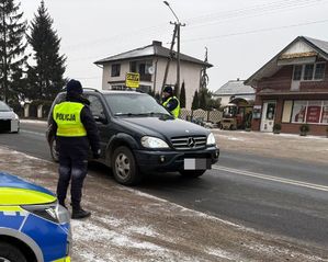 policjant stoi przy drodze a w tle przejeżdża samochód