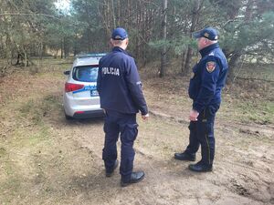strażnik i policjant stoją przy radiowozie w terenie leśnym