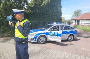 policjant stoi przy drodze w tle radiowóz