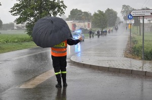 strażak zabezpiecza drogę a w tle w deszczu radiowóz i rowerzyści