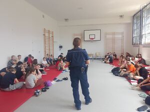 policjantka stoi przed uczestnikami na sali gimnastycznej