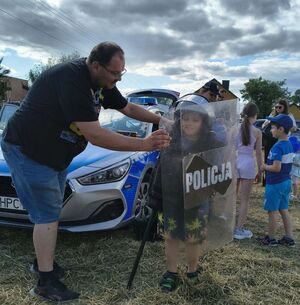 mężczyzna z dzieckiem trzymającym tarcze w kasku i kamizelce "Policja"