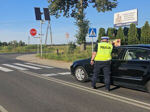 policjant stoi przy aucie i sprawdza stan trzeżwości