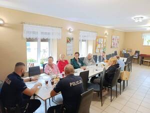siedzą przy stole dzielnicowi i rozmawiają z seniorami